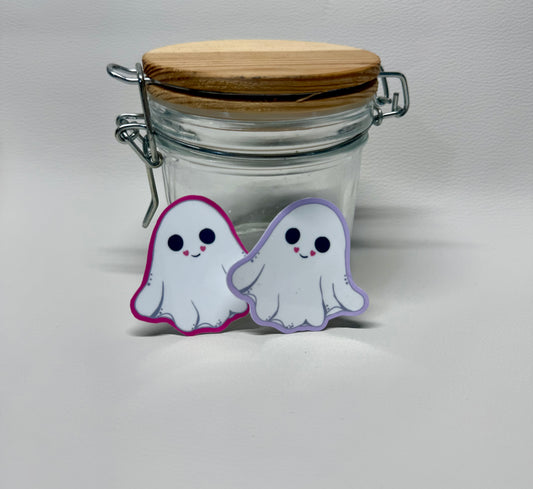 Displayed are two 2-inch die-cut stickers. They are cute ghost-shaped stickers with smiling faces, with hearts in the corners of the smiles. One variation is outlined in hot pink and the other in light purple.